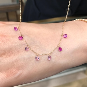 Peut inclure: Un collier délicat en chaîne dorée avec des accents de pierres précieuses roses. Le collier présente une série de petites pierres précieuses roses rondes qui pendent de la chaîne.