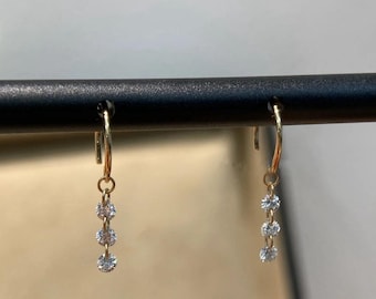 May include: A pair of gold dangle earrings with three small round diamonds hanging from each earring.