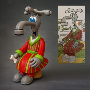 May include: A whimsical sculpture of a faucet-headed character wearing a red robe with green stripes and trim, holding a bone. The character has a surprised expression and blue eyes. A drawing of the character is on the right.