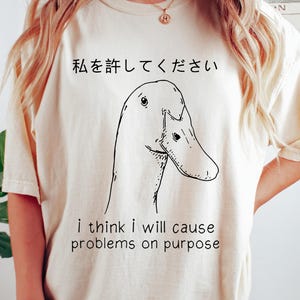 May include: A cream colored t-shirt with a black and white illustration of a duck. The text "私を許してください" and "i think i will cause problems on purpose" is printed on the shirt.