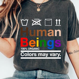 May include: A gray t-shirt with the text "Human Beings" in rainbow colors. The text "100% Organic" and "Colors may vary." are also printed on the shirt.