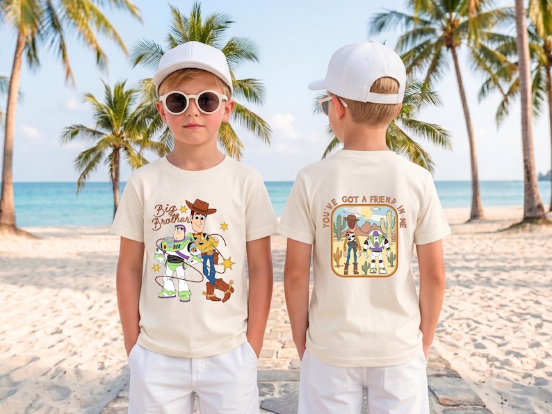 May include: A cream-colored short-sleeve t-shirt featuring a graphic of Woody and Buzz Lightyear on the front with the text Big Brother. The back displays a desert scene with the characters and the text You've Got A Friend In Me.