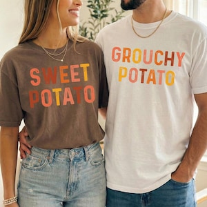 Könnte beinhalten: Ein dunkelbraunes T-Shirt mit dem Text SWEET POTATO in Orange, Gelb und Pink sowie ein weißes T-Shirt mit dem Text GROUCHY POTATO in Orange, Gelb und Pink. Beide T-Shirts haben kurze Ärmel und einen Rundhalsausschnitt und werden zu blauen Jeans getragen.