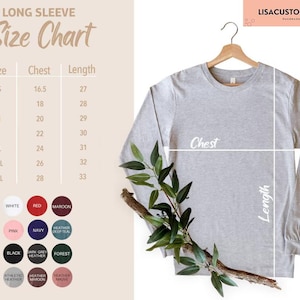 May include: A light gray long-sleeve shirt hanging on a wooden hanger, with a size chart to the left. The size chart shows chest and length measurements in inches. Color swatches are displayed below the size chart.