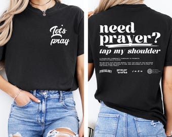 Puede incluir: Camiseta negra con el texto "Let's pray" en la parte delantera y "Need prayer? Tap my shoulder" en la parte trasera. La camiseta también presenta texto adicional que promueve la oración. La camiseta se combina con vaqueros azules.