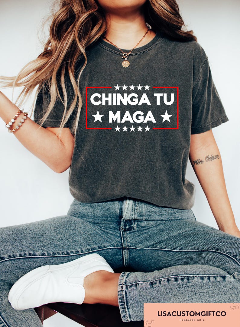 May include: Dark grey t-shirt featuring the text "CHINGA TU MAGA" in a white box with a red border, and stars above and below. The shirt is a casual style.