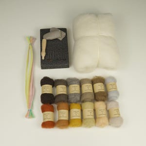 Puede incluir: Un kit de manualidades para fieltrar con aguja que contiene un bloque grande de lana cardada blanca, una base de espuma negra, una herramienta de madera, varias agujas de metal, limpiapipas de colores y doce ovillos de lana en tonos tierra.
