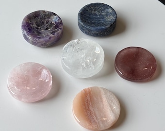 May include: An assortment of polished gemstones in various colors, including amethyst, rose quartz, and a reddish-brown stone. The gemstones are round and flat, with a smooth, reflective surface. Some have a slight concave shape.