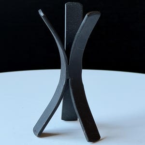 May include: A matte black metal display stand featuring a vertical central spine with two curved, outward-extending arms on each side. The structure is composed of flat, intersecting metal strips that form a stable base with four points of contact.