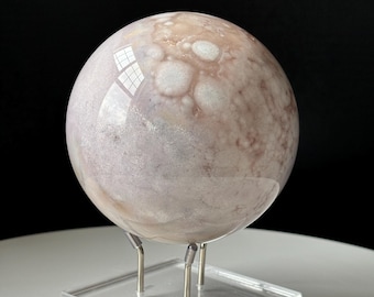 May include: A polished, white and pink agate sphere with a swirling pattern sits on a clear acrylic stand with three metal legs.
