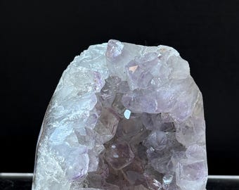 Könnte beinhalten: Eine große Amethyst-Geode mit einem hohlen Zentrum, das mit kleineren Amethyst-Kristallen gefüllt ist. Die Geode ist hellviolett und hat eine glatte, polierte Oberfläche.