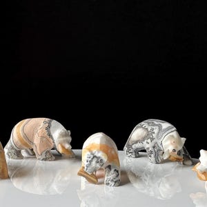 May include: Six carved stone bear figurines in various poses. The bears are made of stone with colors ranging from cream, tan, and gray. The bears are on a white surface with a black background.