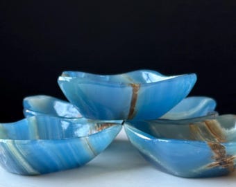 May include: Four blue onyx bowls with a wavy rim are stacked. The bowls have a translucent appearance with streaks of brown and white. The bowls are a decorative item, suitable for serving snacks or as a display piece.