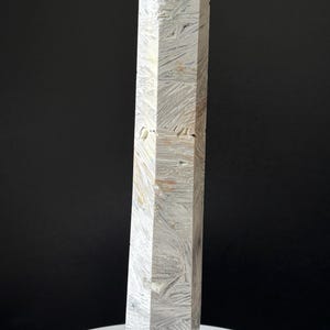May include: A tall, geometric obelisk with a textured, white and gray surface. The obelisk has a pointed top and is set against a black background. The object is likely a decorative item or sculpture.