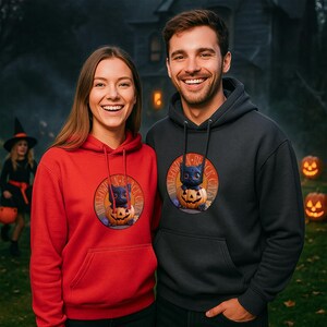 Puede incluir: Dos personas con sudaderas rojas y gris oscuro con un diseño de Halloween. El diseño presenta un gato negro dentro de una calabaza tallada con el texto "Halloween Black Cats" en un diseño circular. Un niño con disfraz de bruja está en el fondo.