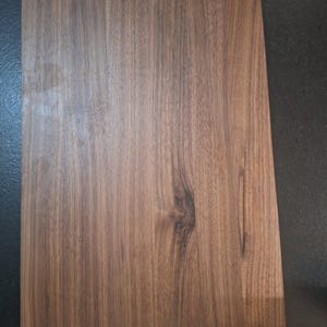 Puede incluir: Primer plano de una lámina de laminado de imitación de madera con un patrón de madera marrón y marrón oscuro. La lámina tiene un acabado liso y brillante.
