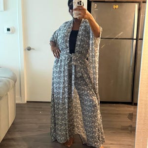 Op de afbeelding: Een lange, vloeiende outfit met zwart-wit patroon. De outfit bestaat uit een bijpassende kimono-achtige top met wijde mouwen en een strikceintuur, gecombineerd met een broek met wijde pijpen. De outfit wordt gedragen over een zwarte top.