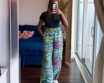 Könnte beinhalten: Weite Hose mit einem lebendigen, mehrfarbigen Muster in Türkis, Gelb, Rosa und Weiß. Die Hose hat eine hohe Taille und eine fließende Silhouette. Die Person trägt ein schwarzes Oberteil und weiße Turnschuhe.