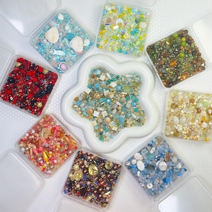 Peut inclure: Une collection de huit boîtes carrées en plastique transparent remplies de perles colorées assorties et un récipient central en forme d'étoile blanche contenant un mélange de perles bleues, dorées et blanches. Les boîtes carrées contiennent des perles rouges, bleues, vertes, jaunes, roses et brunes.