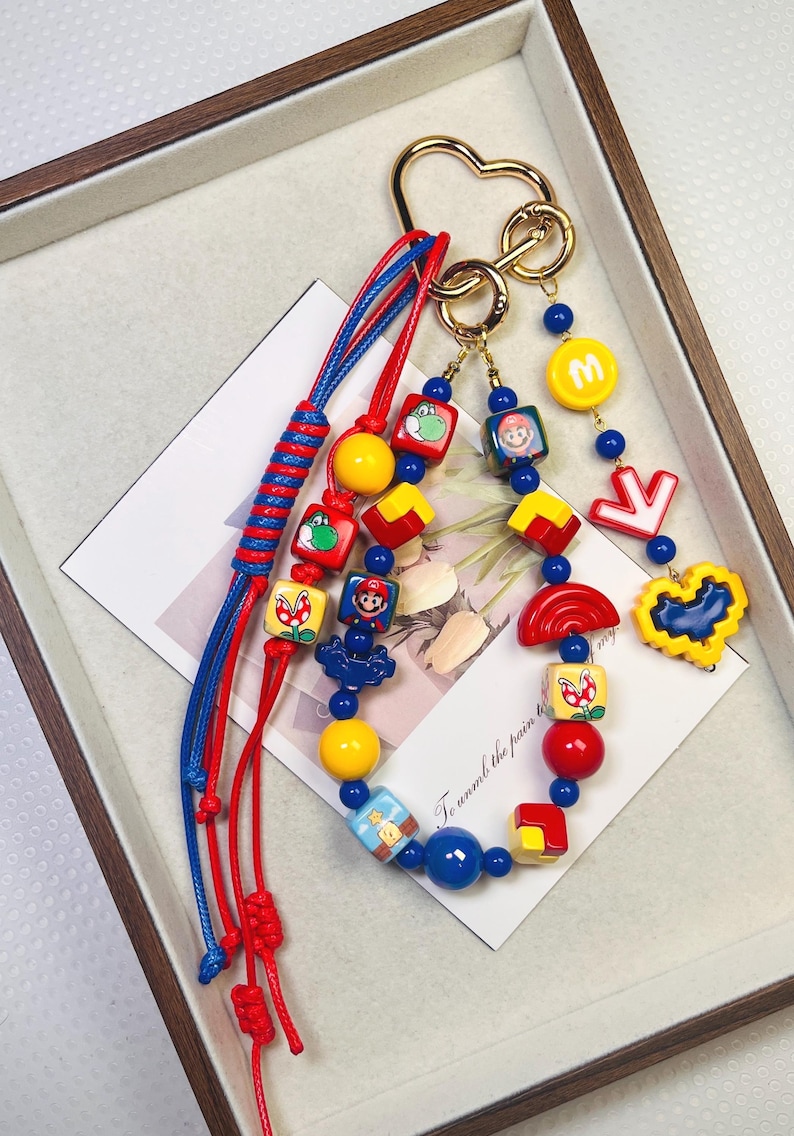 May include: A colorful keychain featuring various cartoon character charms. The keychain includes red and blue cords, gold-colored hardware, and a variety of charms in yellow, red, and blue. The charms depict characters and symbols.