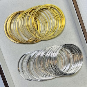 May include: Two sets of wire rings in a tray. One set is gold-coloured, and the other is silver-coloured. The rings are arranged in neat stacks, suggesting they are for jewellery making or crafting. The tray has a light grey interior and a wooden frame.