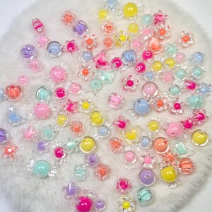 May include: A collection of assorted colorful acrylic beads in various shapes including flowers, stars, and candy-like forms. The beads feature translucent and opaque finishes in shades of pink, yellow, blue, purple, orange, and green.