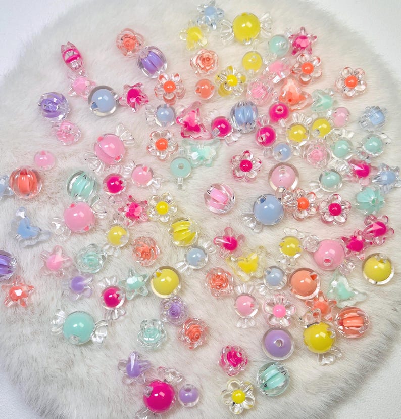May include: A collection of assorted colorful acrylic beads in various shapes including flowers, stars, and candy-like forms. The beads feature translucent and opaque finishes in shades of pink, yellow, blue, purple, orange, and green.