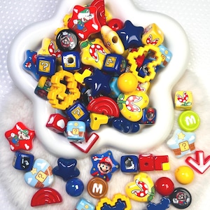 May include: A collection of colorful, themed beads in a white, star-shaped bowl. The beads feature various shapes and designs, including stars, cubes, and hearts, with images of a popular video game character and related icons. The color palette includes red, yellow, blue, and green.