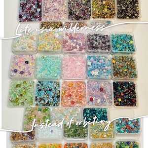 Op de afbeelding: Een verzameling kleine, doorzichtige plastic containers gevuld met diverse kleurrijke kralen, pailletten en glitter. De tekst "Life is a wilderness" en "Instead of orbiting" staat op de afbeelding. De containers zijn in een rasterpatroon gerangschikt.