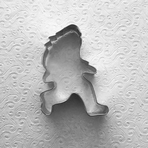 May include: A metal cookie cutter shaped like a person running. The cutter is silver and has a smooth surface.