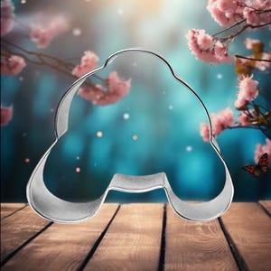 May include: A silver metal cookie cutter shaped like a car, sitting on a wooden surface. The background is a blurred image of pink flowers and a blue sky.
