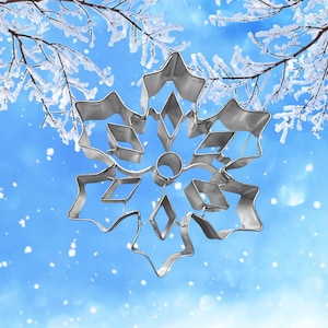 May include: A silver snowflake cookie cutter against a blue and white snowy background.
