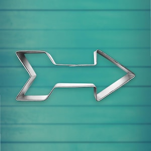 May include: A silver metal arrow-shaped cookie cutter on a teal blue wooden background.