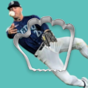 May include: A silver metal cookie cutter shaped like a baseball glove. The cutter has a detailed design with a scalloped edge.