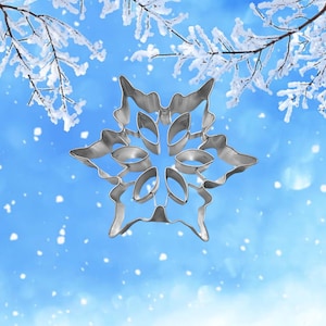 May include: A silver snowflake cookie cutter against a blue and white snowy background.