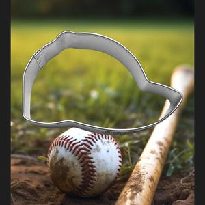 May include: A silver baseball cap cookie cutter on a wooden baseball bat with a baseball in the foreground.