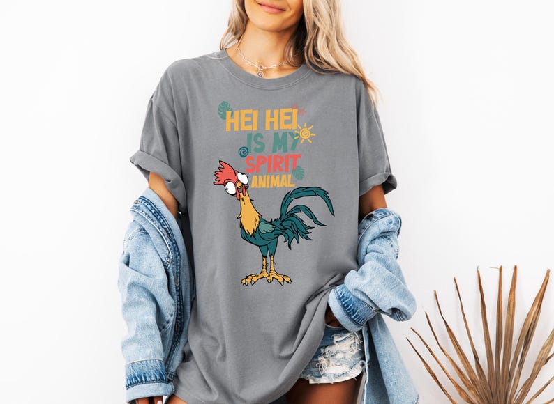 A woman wearing a gray t-shirt with a graphic of a rooster and text, along with denim clothing and a denim jacket.