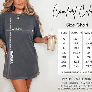 a woman wearing a grey t-shirt with measurements and a size chart for the t-shirt, along with a drink in a glass.