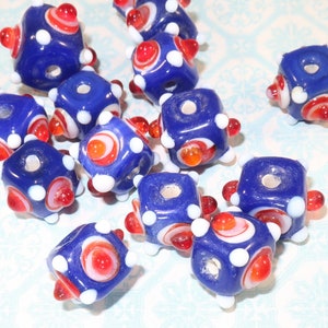May include: A collection of blue glass cube beads with white and red accents. The beads have a hole in the center for stringing.
