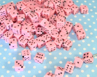 May include: A large pile of pink dice with black dots. The dice are scattered on a blue and white polka dot background. There is a smaller line of pink dice with black dots on the bottom right of the image.