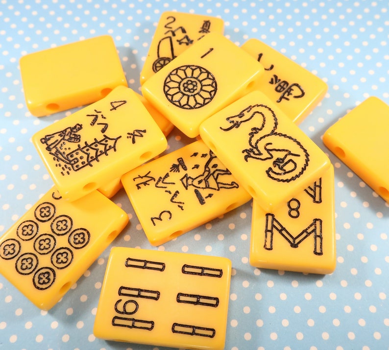 May include: A set of ten yellow mahjong tiles with black Chinese characters and symbols. The tiles are arranged in a random pattern on a blue and white polka dot background.