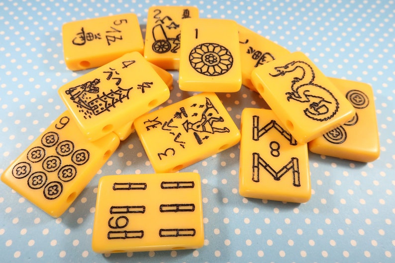 May include: A collection of yellow mahjong tiles with black markings. The tiles feature various symbols and numbers, including a dragon, bamboo, and circles.