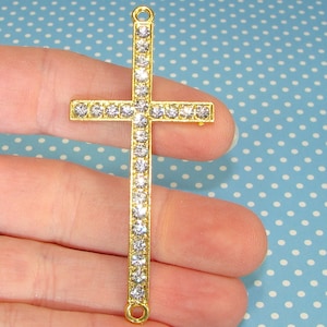 May include: A gold-tone cross pendant with clear rhinestones. The cross is about 2 inches long and has a loop at the top for attaching to a chain.