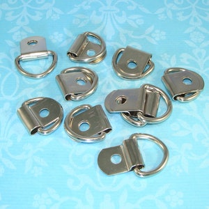 May include: Ten silver-toned metal D-rings with a flat back and a hole in the center. The D-rings are arranged in a random pattern on a light blue background.