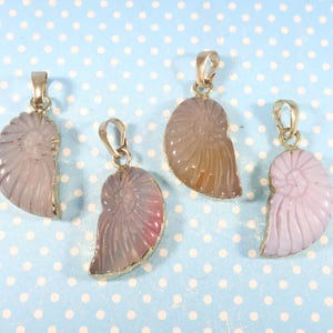 Peut inclure: Quatre pendentifs en forme de coquille de nautile en pierre sculptée dans des tons rose clair, lavande et beige. Chaque pendentif est monté sur une monture en métal doré avec une bélière assortie, présentant un motif en spirale strié.