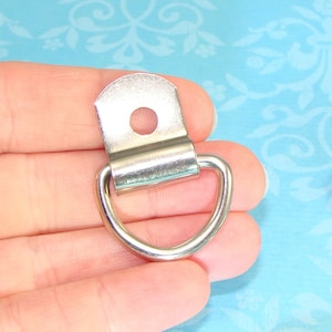 May include: Silver metal D-ring with a flat plate and a hole for attaching to a surface. The D-ring is about 1 inch in diameter.