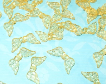 May include: A collection of translucent yellow mermaid tail charms. Each charm features a detailed tail fin design. The charms are scattered on a light blue surface, creating a whimsical and decorative effect.