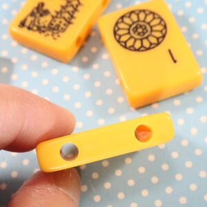 May include: A yellow plastic tile with two round holes. The tile is a game piece for a board game.