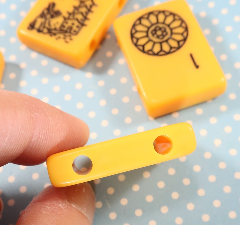 May include: A yellow plastic tile with two round holes. The tile is a game piece for a board game.