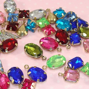 May include: Assortment of colorful glass and crystal charms with gold-tone metal settings. The charms are shaped like ovals, squares, and teardrops. They are perfect for jewelry making or crafting.